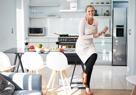 I found just the recipe. a mature woman using her digital tablet while wearing her apron in the kitchen.の写真素材