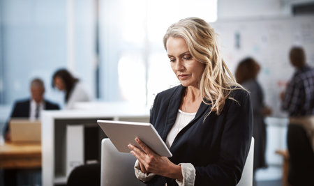 Digital technology really does help to optimize productivity. a mature businesswoman using a digital tablet in an office.の写真素材