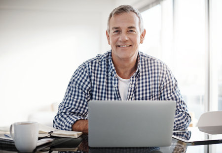 I always use technology to catch up with current affairs. Portrait of a mature man working on a laptop at home.の写真素材