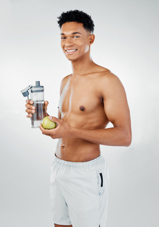 Fitness, apple and man drinking water in studio after training, cardio workout and exercise for body wellness. Lifestyle, fruit and healthy young athlete or happy personal trainer on a vegan dietの写真素材