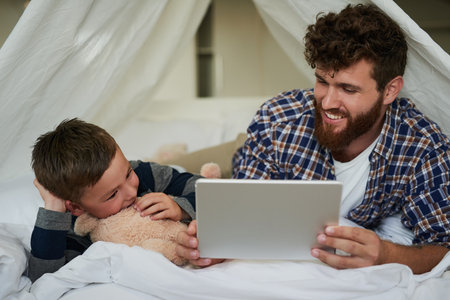 Check this out. a handsome young man and his son using a tablet while lying on the bed at home.の写真素材