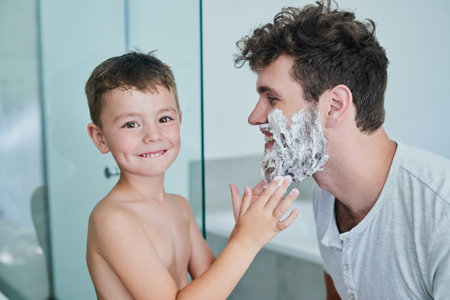 Im getting Dad ready for a clean shave. Portrait of a little boy rubbing shaving cream on his fathers face in the bathroom at home.の写真素材