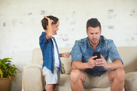 Doing everything to get some attention. a man busy on his phone while his son is seeking for attention.の写真素材