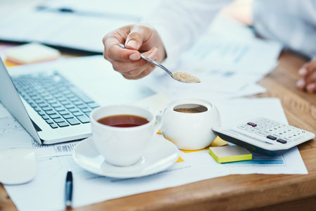 Adding some sweetener to his drink. an unrecognizable businessman pouring a teaspoon of sugar into a cup of tea in an office.の写真素材
