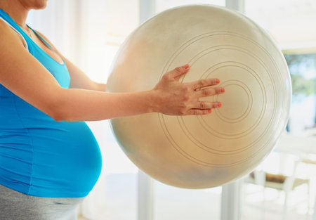 Shes on the ball with her pregnancy workout routine. a pregnant woman working out with an exercise ball at home.の写真素材