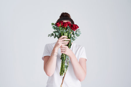 Flowers are loves truest language. Studio shot of an unrecognizable woman covering her face with flowers against a grey background.の写真素材