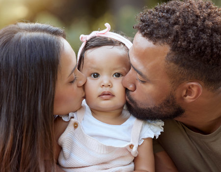 Mother, father and baby face kiss while bonding in a garden outdoors with love, care and affection. Loving, caring parents kissing little daughter while bond in nature for calm relaxationの写真素材