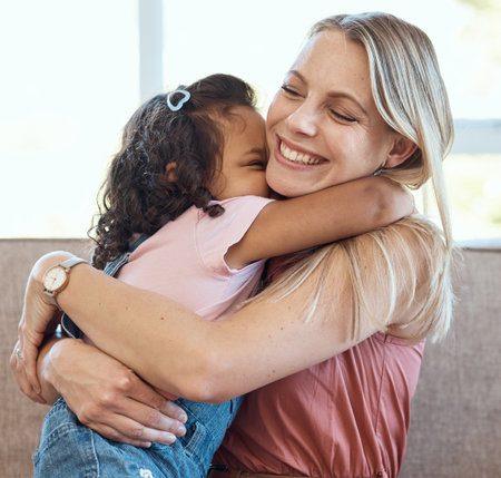 Mother, hug and child love on a home living room sofa feeling interracial family and kid care. Mama, happy girl and parent loving her kid with a smile on a house lounge couch hugging in a family homeの写真素材