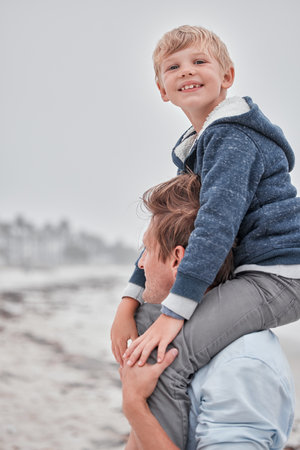Beach, portrait of dad and child on shoulders with smile on family holiday or cloudy ocean walk in Australia. Travel, fun and happy father and son playing and walking at sea on vacation with gray skyの写真素材