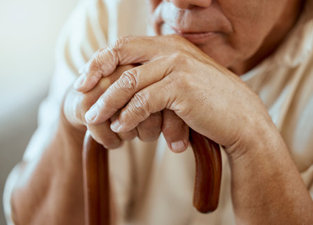 Hands of elderly man on walking stick, serious and sitting thinking, memories at retirement home. Grandpa with wooden cane, senior care for disability and nostalgia for sad lonely guy at nursing homeの写真素材