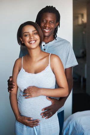 The smiles on our faces say it all. Portrait of happy young man posing with his pregnant wife at home.の写真素材