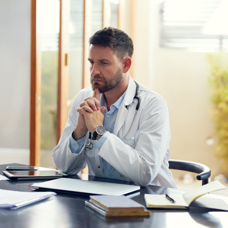 Hes got a lot to think about. a handsome male doctor looking thoughtful while sitting in his office.の写真素材