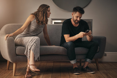 Has the trust disappeared from their marriage. a young woman looking at what her husband is doing on his phone.の写真素材
