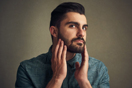 Dont be the same, be someone with a beard. a handsome young man touching his beard against a grey background.の写真素材