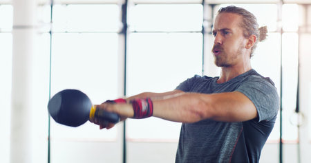 Whether in life or gym, go hard. a young man working out with kettle bells in a gym.