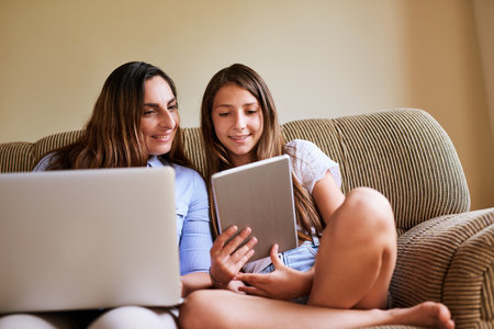 Thats interesting my dear. a cheerful young women and her young daughter browsing on a laptop and digital tablet while being seated on a sofa at home.の写真素材