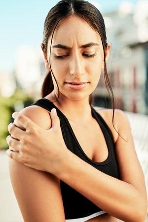 Just what Ive been fearing. a sporty young woman holding her shoulder in pain while exercising outdoors.の写真素材