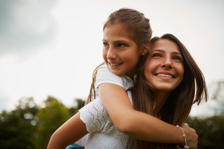 Sisters are there to support one another. a young girl giving her younger sister a piggyback ride outdoors.の写真素材
