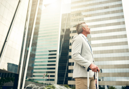 Welcome to the city full of great big dreams. a mature businessman walking with a suitcase in the city.の写真素材