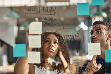 Two young designers brainstorming with notes on a glass wall in an office.