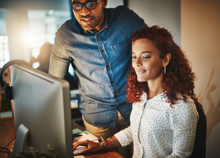A young businessman and businesswoman using a computer together during a late night at work.の写真素材