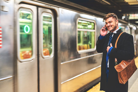 Time to hop on the train. a cheerful young man talking on his phone while waiting for a train to get to work in the morning.の写真素材