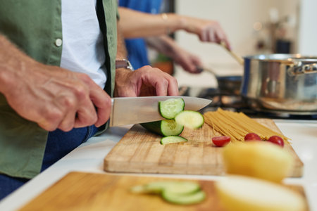 Preparing all the ingredients they need. Closeup shot of an unrecognizable man slicing cucumbers while cooking with his wife at home.の写真素材