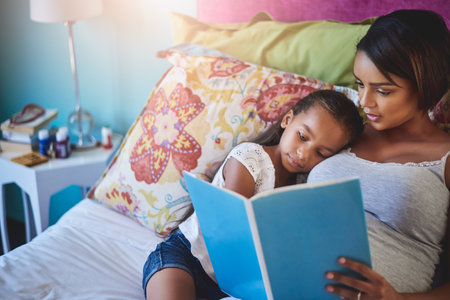 Spark their imagination through the world of magical words. a mother reading a story to her little daughter at home.の写真素材