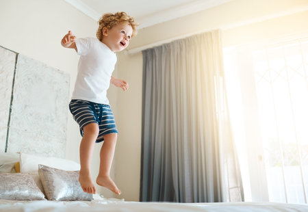 Jumping for joy. an adorable little boy jumping on the bed at home.の写真素材