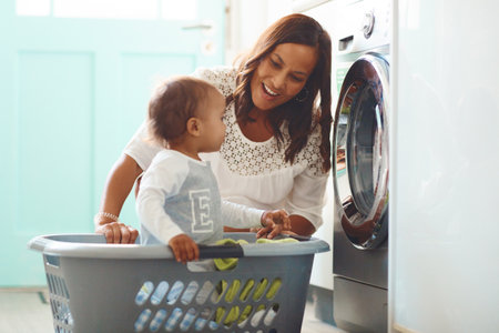Hes such a curious little one. a mother and her adorable baby boy doing the laundry at home.の写真素材