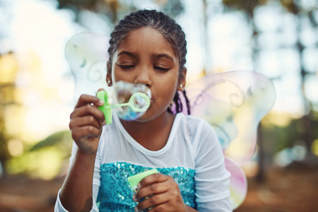 Kids will be kids. a little girl dressed up as a fairy and playing with bubbles in the woods.の写真素材