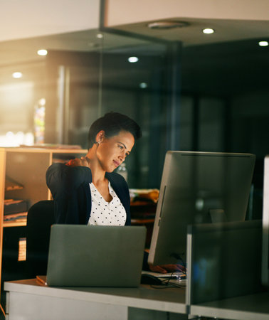 Feeling the tension of a long workday. a young businesswoman suffering with neck pain while working late in an office.の写真素材