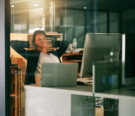 I did well today. a young businesswoman taking a break while working late in an office.の写真素材