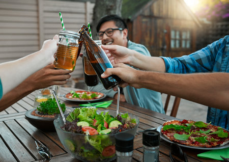 Cheers everyone. a group of young friends holding up drinks and toasting outside around a table to celebrate their friendship.の写真素材