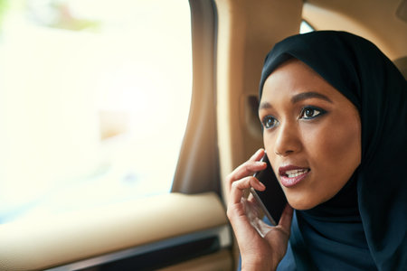 Thanks for calling. a focused young businesswoman talking on her mobile phone while being seated in the back of a car on her way to work.の写真素材