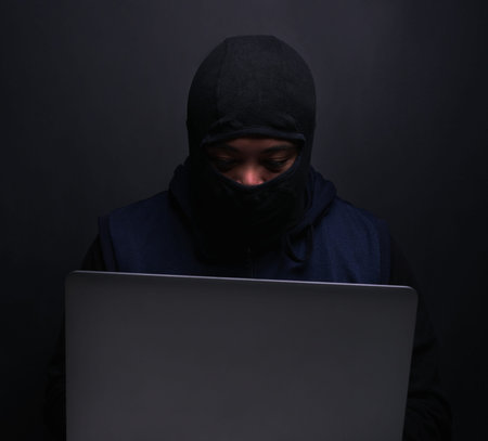 Doing some shady things. a hacker using a laptop against a dark background.