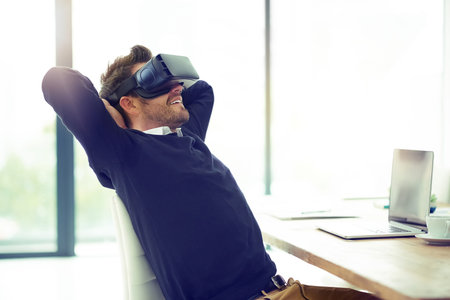 Business and relaxation done in one. a businessman wearing a VR headset while leaning back in his...