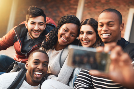 Keep your college friends close. a group of students taking selfies together on campus.の写真素材