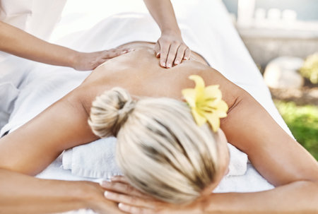 Nothing better to relieve the stress of work. a relaxed middle aged woman lying on her stomach while receiving a massage at a spa outside during the day.の写真素材