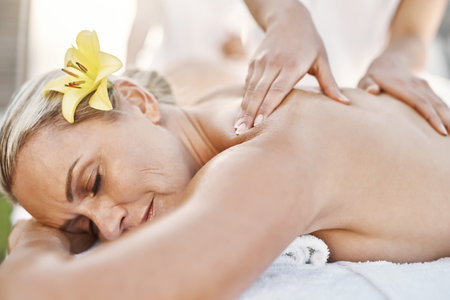 I can stay like this the whole day. a relaxed middle aged woman lying on her stomach while receiving a massage at a spa outside during the day.の写真素材
