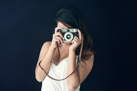 Everything has beauty but not everyone sees it. a beautiful young holding a camera against a dark background.の写真素材