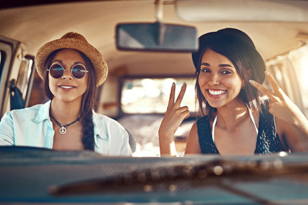 Ready for whatever the road brings. two happy friends showing a peace sign on a roadtrip.の写真素材