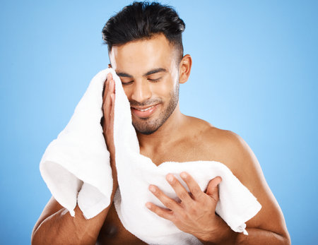 Beauty, skincare and shower with man and towel for facial, product and wellness morning routine. Happy, clean and hygiene with model against blue background for health, fresh and cosmetics lifestyleの写真素材