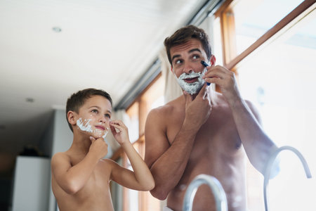 A handsome young man teaching his son how to shave in the bathroom.の写真素材