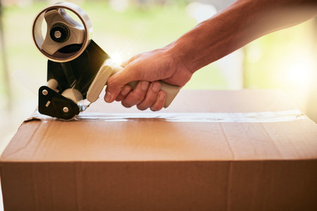 All packed up and ready to go. Closeup shot of an unrecognizable man closing a cardboard box with tape.の写真素材