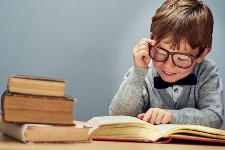 Nothing grows a mind like knowledge. Studio shot of a smart little boy reading books against a gray background.の写真素材