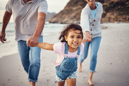 Family, beach and grandparents holding hands of girl on vacation, holiday or summer trip. Love, care and grandma, grandpa and happy kid enjoying quality time together, bonding and running on seashoreの写真素材