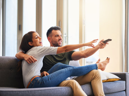The battle of choosing what to watch. a young couple fighting over the remote control while watching tv at home.の写真素材
