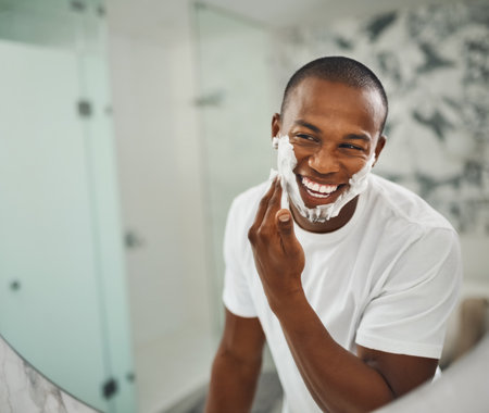 A handsome young man shaving his facial hair in the bathroom.の写真素材