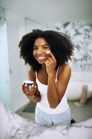 I only give my skin the best. Portrait of an attractive young woman applying moisturizer to her face at home.の写真素材